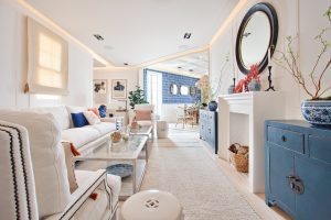 Espacio “El Ático” de El Corte Inglés en Casa Decor 2022, salón luminoso con sofá blanco, muebles en azul y detalles decorativos en un ambiente de estilo mediterráneo.
