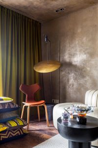 Detalle del espacio «Gylden æske», diseñado por COMAD Arquitectos para Danish Design+ en Casa Decor Madrid 2023, con una silla Grand Prix de Arne Jacobsen, lámpara de pie y acabados en tonos cálidos.