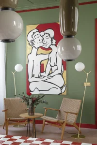 Dos butacas CH25 de Hans J. Wegner en el espacio «Dos vidas en un baño», diseñado por Lieve Studio para Jacob Delafon en Casa Decor 2025, con pared verde oliva y suelo de damero rojo y blanco.