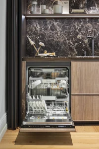 Lavavajillas integrado de Miele en cocina diseñada por Equipo Santos en Casa Decor 2025, con mobiliario en madera y encimera de piedra oscura.
