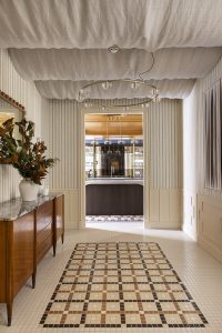 Entrada de loft en Casa Decor 2026 con suelo de mosaico geométrico, molduras en paredes y mobiliario de madera