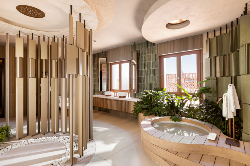 Baño wellness con jacuzzi circular y celosía metálica dorada, diseño de Estudio Querencia para Nais en Casa Decor 2026, con cerámica, madera y vegetación interior