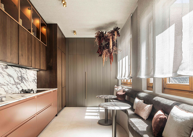 Cocina de diseño en acabado cobre y burdeos de Espacio BAUHAUS con encimera Sapienstone efecto mármol, iluminación suave y zona office integrada con banco tapizado.