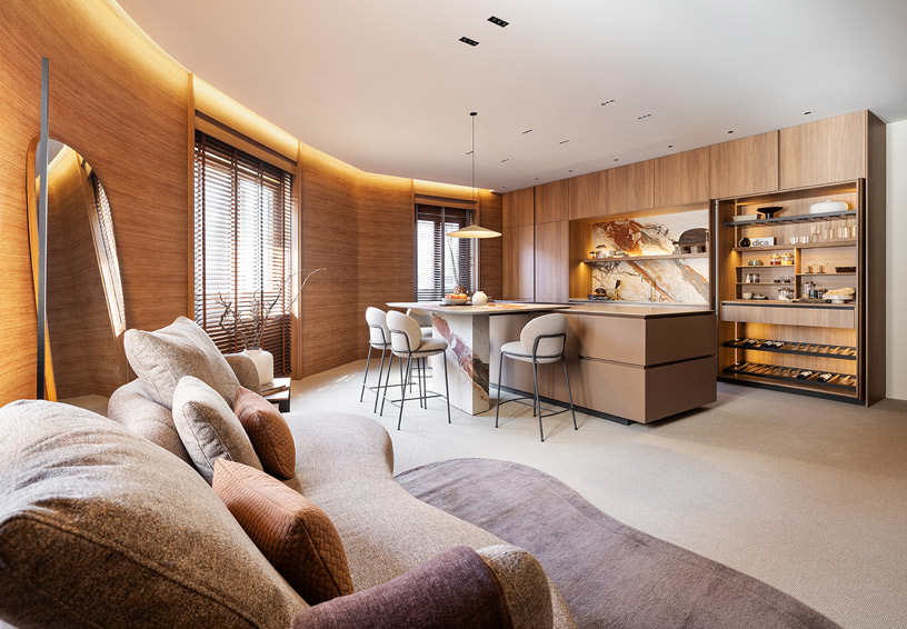 Cocina abierta de Dica integrada en el salón con isla funcional, muebles de madera, encimera Inalco y zona de estar con sofá, ejemplo de diseño de cocina multifuncional.