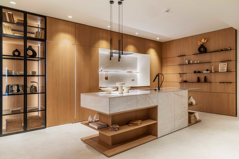 Cocina minimalista de Doimo Cucine con líneas limpias, madera natural, isla con revestimiento efecto mármol de Florim y estanterías abiertas, estilo moderno y cálido.