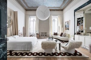 Suite italiana con cama blanca, lámpara esférica de papel, chimenea y zona de estar, diseñada por Rebuelta Domecq para Casa Decor 2026.