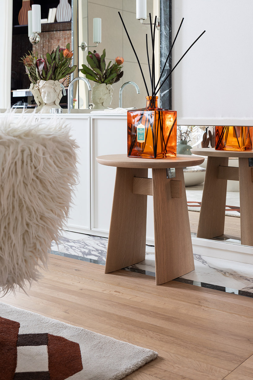 Detalle decorativo con difusor Pernici sobre mesa auxiliar, interiorismo italiano con textiles y acabados en madera en Casa Decor