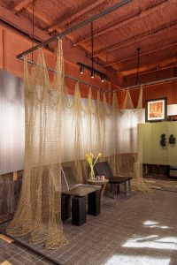 Rincón de conversación de Dos Latitudes con cortinas translúcidas, banco y mobiliario verde en Casa Decor 2026