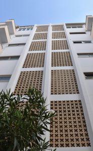 Fachada blanca con paños de celosía de terracota y vegetación exterior