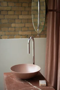 Lavabo de diseño con grifería metálica y acabados en tonos terracota en el espacio Kaldewei