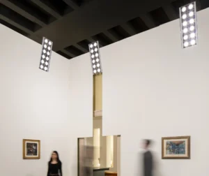 Sistema de iluminación Cestello, desarrollado por Gae Aulenti y Piero Castiglioni para el Palazzo Grassi de Venecia, con proyectores rectangulares suspendidos del techo, múltiples focos orientables y luz dirigida hacia las obras de arte expuestas en paredes blancas.