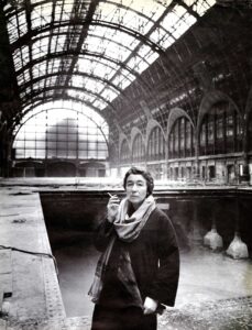 Fotografía en blanco y negro de Gae Aulenti durante las obras de transformación de la estación Gare d’Orsay de París en 1980, con la gran bóveda acristalada de hierro, los arcos de la antigua estación y las estructuras en construcción al fondo.